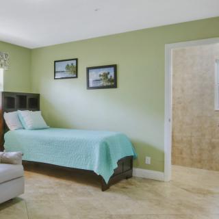 A cozy bedroom featuring a single bed with a turquoise cover, green walls, and minimalist decor.