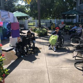 People enjoying a sunny day outside in wheelchairs under garden umbrellas.