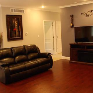 A cozy living room with a leather sofa, television, and hardwood flooring.
