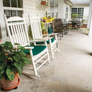 A peaceful porch with white rocking chairs and potted plants, perfect for relaxation.