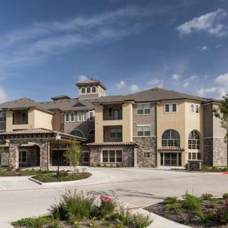 A modern apartment complex with a mix of stone and stucco exterior under a clear blue sky.