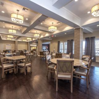 A spacious dining area with multiple round tables, chairs, and elegant ceiling lights.