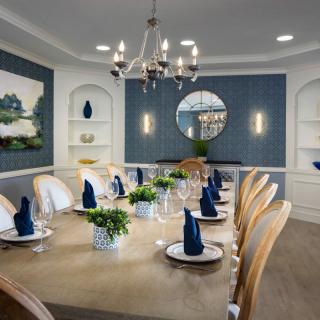 An elegantly set dining room featuring a large table with blue napkins, a chandelier, and stylish wall decor.