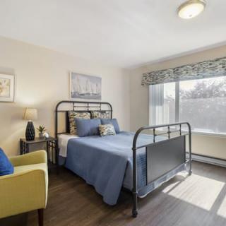 A cozy bedroom with a metal bed frame and blue bedding, illuminated by natural light from a large window.