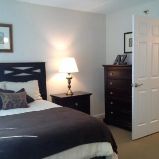 A cozy bedroom featuring a neatly made bed, a bedside lamp, and a dresser.