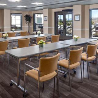 A modern meeting room with neatly arranged tables and chairs, illuminated by natural light from large windows.