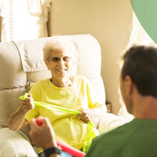 An elderly woman smiles while engaging in a therapy session with a caregiver.