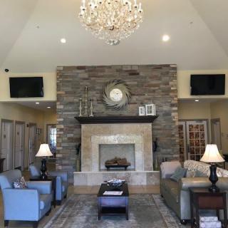 A cozy living room with a large stone fireplace, elegant chandelier, and plush seating.