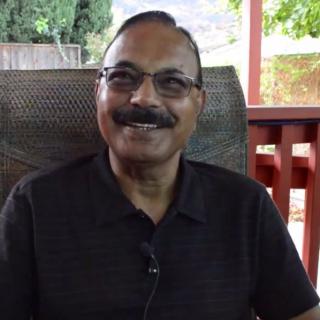 A man wearing glasses is smiling while seated outdoors.