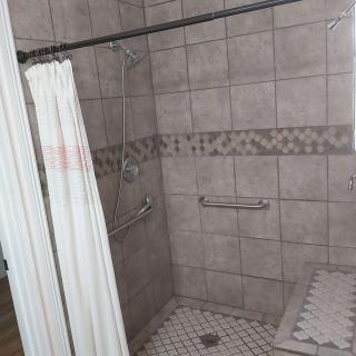 A tiled bathroom shower with a curtain and grab bars for accessibility.