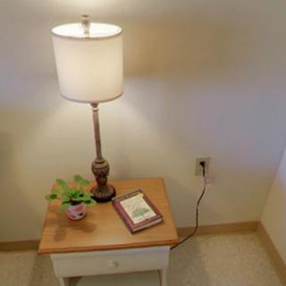 A cozy corner with a lamp, book, and plant on a wooden side table.