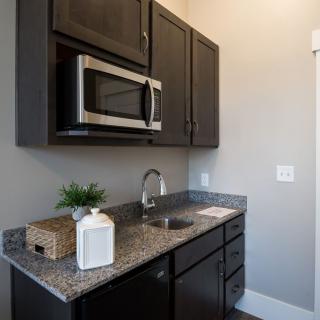 A compact kitchenette featuring dark cabinets, a microwave, and a granite countertop with a sink.