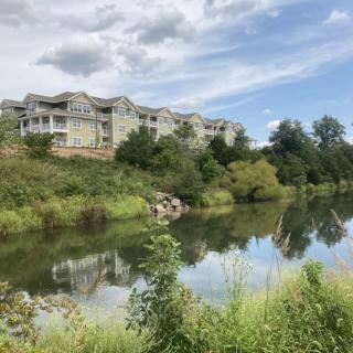 Scenic view of buildings overlooking a serene river with clear reflections and a cloudy sky.