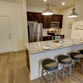A modern kitchen with stainless steel appliances and a marble countertop with bar stools.