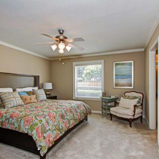 A cozy bedroom with a floral-patterned bedspread, framed artwork on the walls, and comfortable seating by the window.