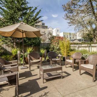 A cozy outdoor patio area with seating and an umbrella, surrounded by greenery.