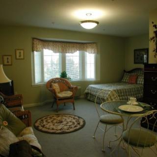 A cozy bedroom with a bed, chair, and table situated near a large window.