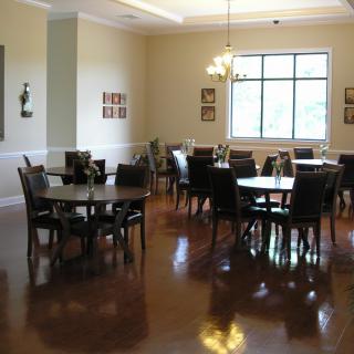 A well-lit dining room with several tables and chairs, featuring hardwood flooring and wall decor.