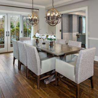 A modern dining room with elegant chandeliers, a large wooden table, and upholstered chairs.