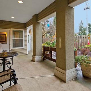 A cozy patio area with seating and plants, sheltered by a roof and supported by columns.
