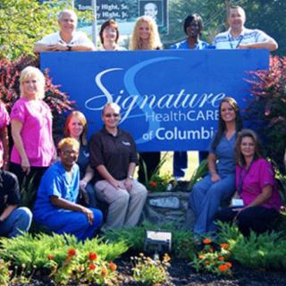 A group of healthcare staff posing with a Signature HealthCARE banner outside.