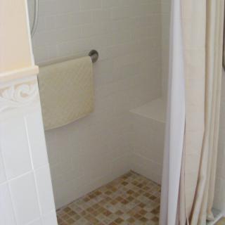 A bathroom shower area with a tile floor, curtain, and towel rack.