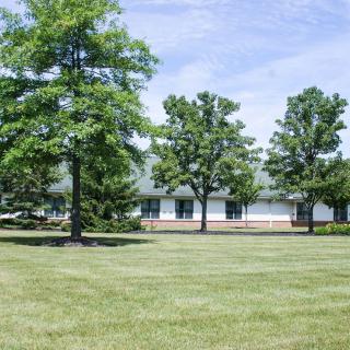 A building surrounded by trees with a green lawn under a clear sky.
