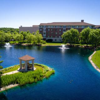 Scenic view of a lakeside area with a gazebo, fountains, and surrounding greenery.