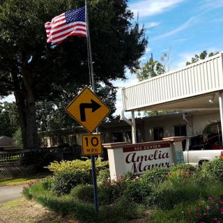 A view of Amelia Manor with an American flag flying and a warning sign indicating a right turn ahead.