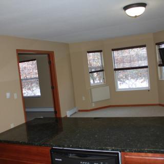 A spacious living room with large windows and a view of the kitchen counter.