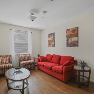 A cozy living room with a red sofa, striped chairs, and a glass coffee table on a wooden floor.
