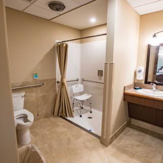 An accessible bathroom featuring a toilet, shower with a chair, and a sink area.
