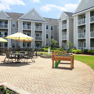 A well-maintained apartment complex courtyard featuring outdoor seating with umbrellas and landscaped surroundings.