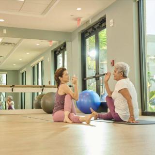 Two women practicing yoga together in a bright, spacious gym.