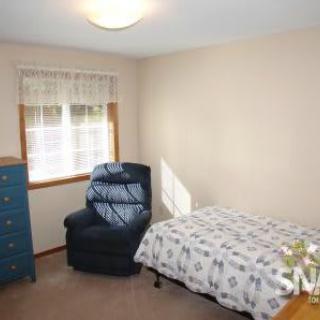 A simple bedroom with a single bed, armchair, and dresser near a window.