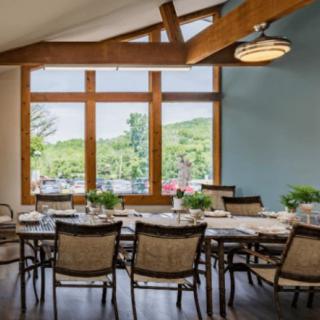 A spacious dining area with large windows and elegant decor, featuring a set table surrounded by chairs.
