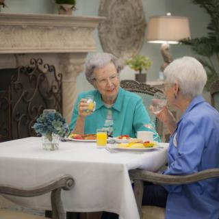 Two elderly women enjoying a meal and conversation at a dining table.