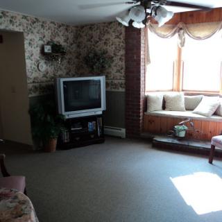 A cozy living room featuring a classic television set, a comfortable window seat, and a ceiling fan.