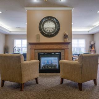 A cozy living room featuring a fireplace, comfortable chairs, and an elegant clock.