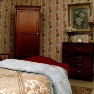 A cozy bedroom featuring vintage wallpaper, a wooden wardrobe, and a matching dresser with decorative items.