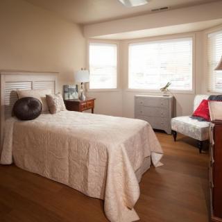 A cozy bedroom with a single bed, armchair, and natural light from the windows.
