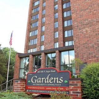 A brick apartment building with a sign in front labeled 'Gardens' and an American flag nearby.