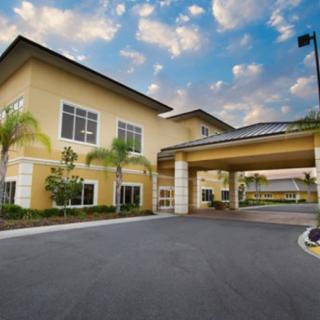 A modern building with a covered entrance and palm trees, set against a cloudy sunset sky.