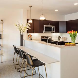 A modern kitchen with sleek design, featuring a countertop with barstools and pendant lighting.