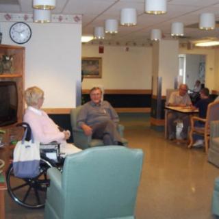 Elderly residents engaging in conversation in a nursing home common area.