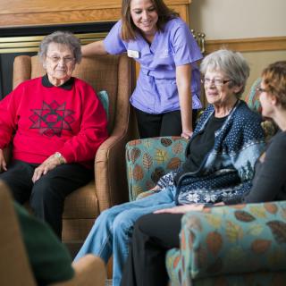 A group of seniors socializing with a caregiver in an indoor setting.