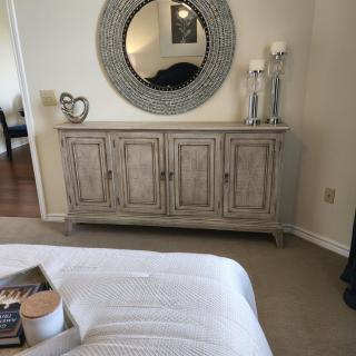 A cozy bedroom featuring a decorative dresser topped with candles and a large round mirror.