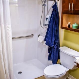 A small bathroom featuring a shower with a grab bar, a toilet, and shelves with bathroom essentials.