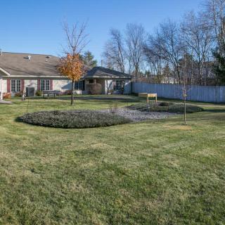A spacious backyard with a well-maintained lawn, surrounded by trees and a white fence under a clear blue sky.