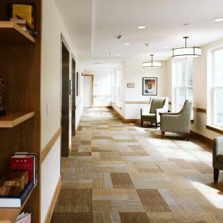 A well-lit hallway with modern decor, featuring comfortable chairs and a bookshelf.